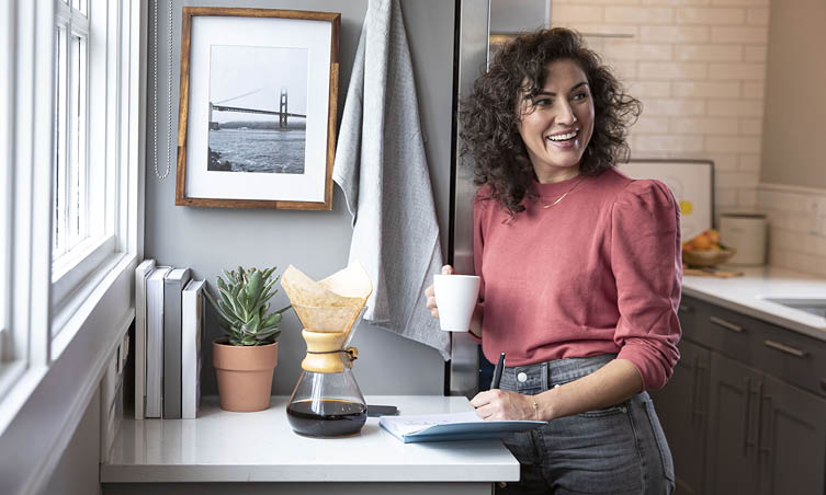 Smiling woman drinking coffee and writing in notebook