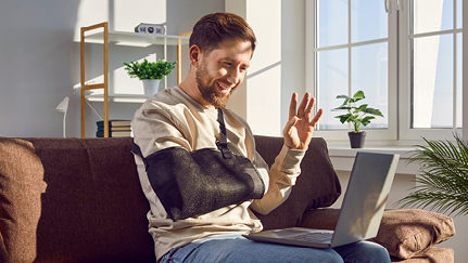 injured worker with arm in sling waves to laptop screen