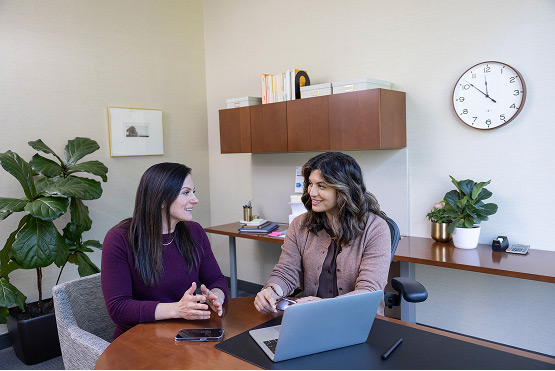 Two employees sit at a table, discussing something on a laptop