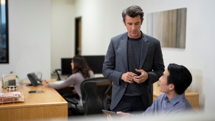 Two men in an office talking at their desks.