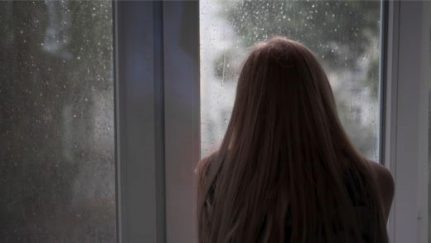A woman looks out a house window during hurricane weather