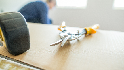 A close-up of a pair of pliers on a wooden surface, with an out-of-focus person in the background.