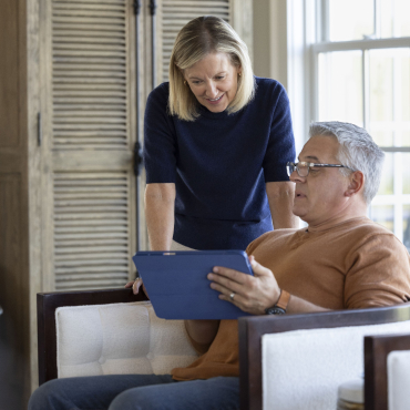 A retirement man checks his email on a tablet and show it to his wife.