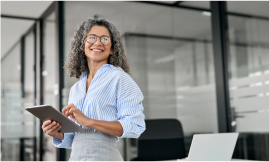 Person standing in an office while holding a tablet and looking away smiling