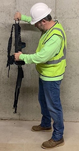 Man holding fall protection harness by the D ring and conducting a visual inspection of the harness